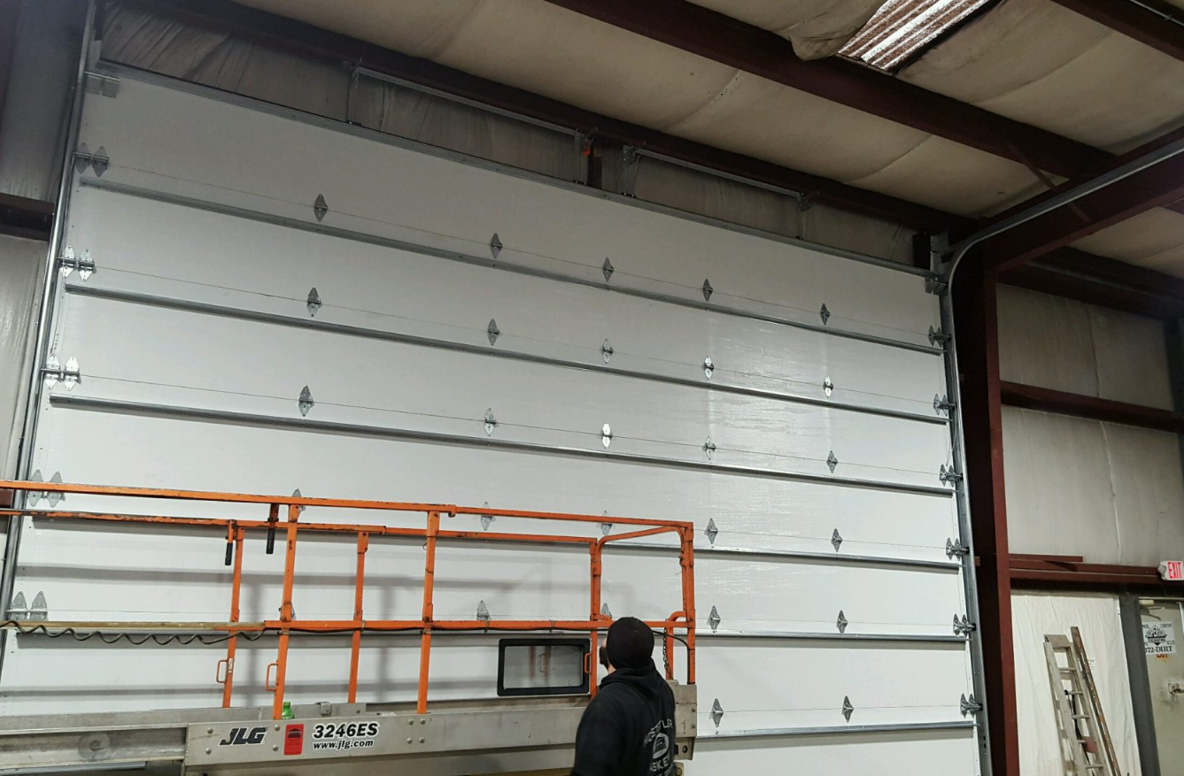 Commercial garage door technician repairing a large metal garage door at a business in Gahanna, Ohio for commercial garage door repair services.